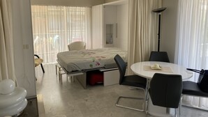 Une chambre d’hôtel moderne comprenant un lit, une table de salle à manger ronde, deux chaises, une lampe et un coin salle de bain.