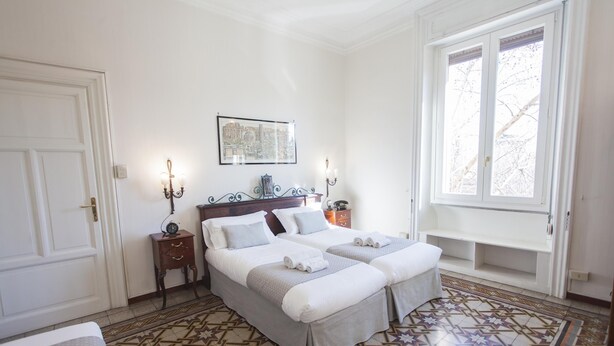 A bedroom with a large bed, a bedside table, a nightstand, a window, and a patterned floor. - ** FAMILY APARTMENT IN TRASTEVERE ** 220sqm -6 bedrooms in the center of ROME!!! (Roma)