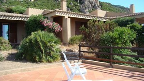 Un patio con sillones blancos de descanso y valla de madera, rodeado de follaje y con montañas al fondo.