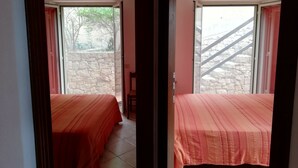 Una habitación con dos camas, una pared de piedra y una escalera que da al exterior.