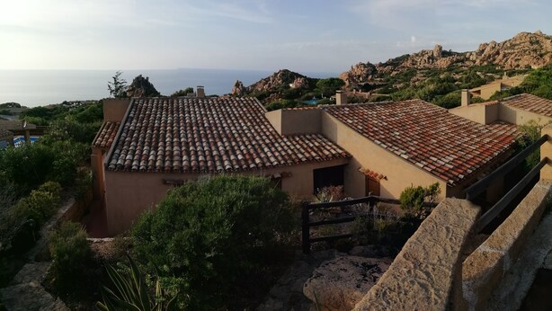 Un barrio residencial con tejados de tejas color terracota, muros de piedra y abundante vegetación.