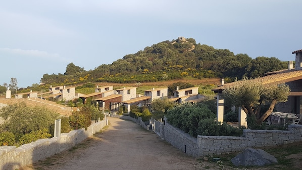 Un pueblo rural con casas de piedra, un camino de tierra y una colina al fondo.