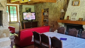 A cozy living room with a stone wall, a wooden balcony, a red sofa, a dining table with chairs, and a television. - mansion - Fournels (Fournels)