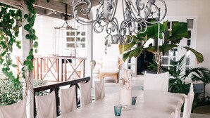 A dining area with a long table, white chairs, and a chandelier. - Very Spacious, Private, Open Plan Retreat. Pool And Stunning Views Of West Coast (Saint Peter)
