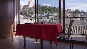 A balcony with a red tablecloth, a bottle, and a glass of wine.