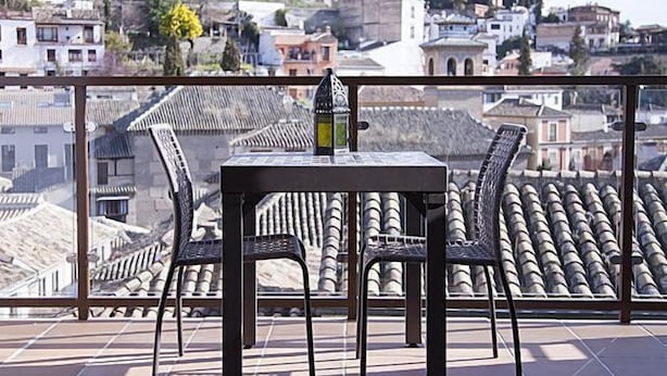 A balcony with a table and chairs, overlooking a cityscape with traditional buildings and a church.