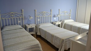 Een kamer met drie eenpersoonsbedden, elk met een witte metalen hoofdbord en een bijpassend nachtkastje.
