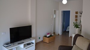 Een woonkamer met een flatscreen televisie op een wit tv-meubel, een rieten mand met bloemen en een bruine bank.