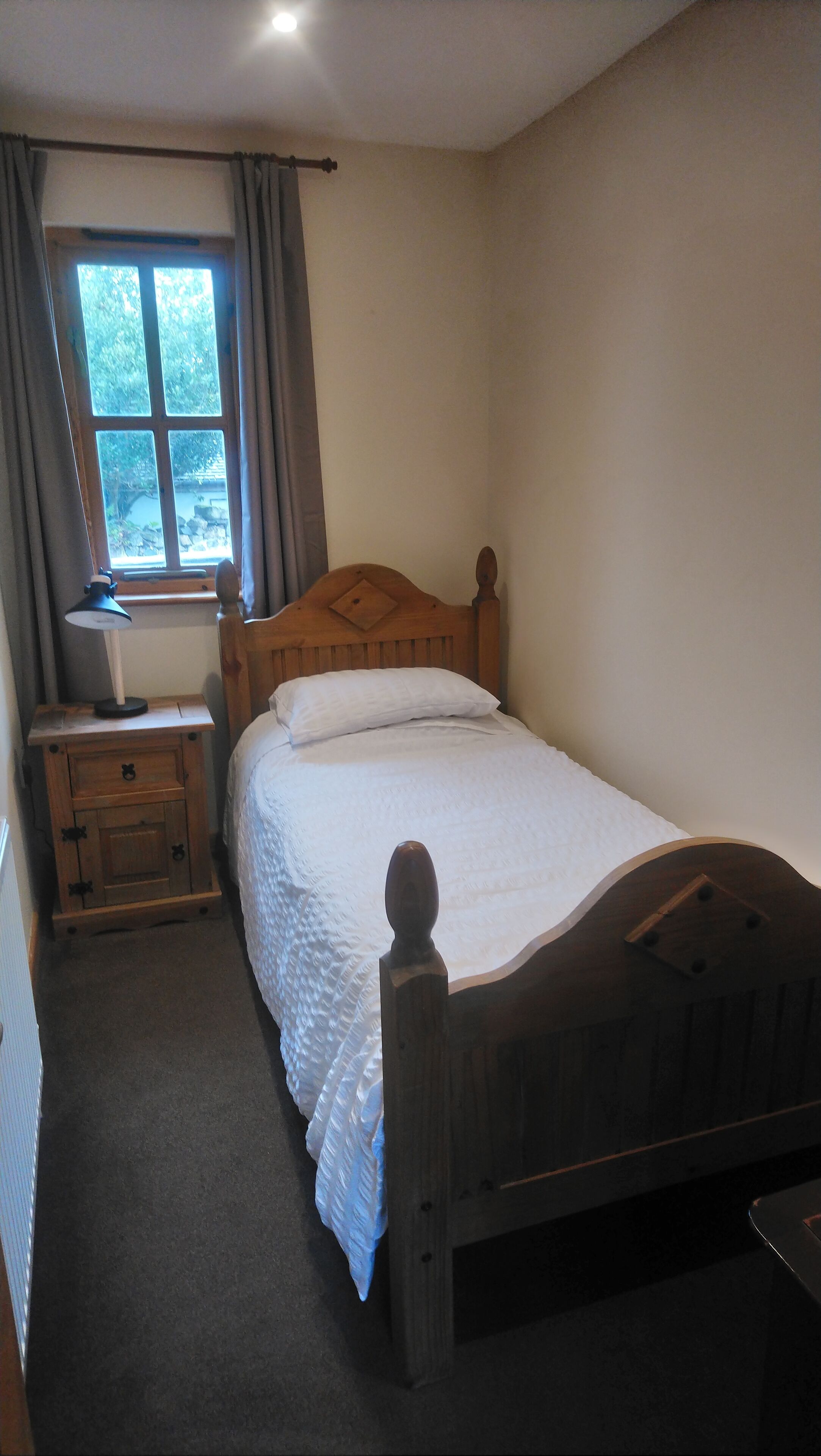 A bedroom with a wooden bed, a nightstand with a lamp, a window with curtains, and a radiator.