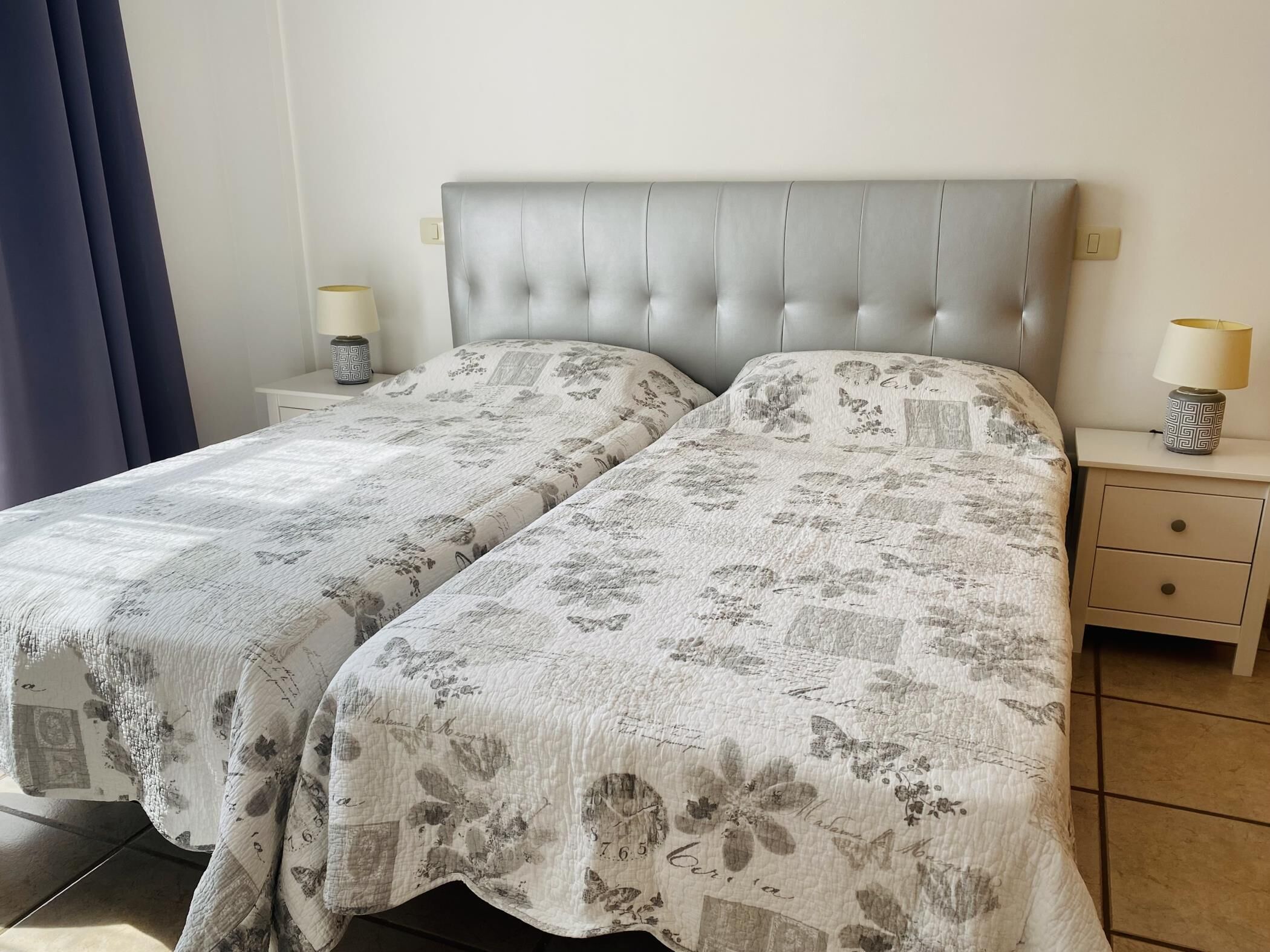 A double bed with a tufted headboard, two bedside tables with lamps, and a patterned bedspread.