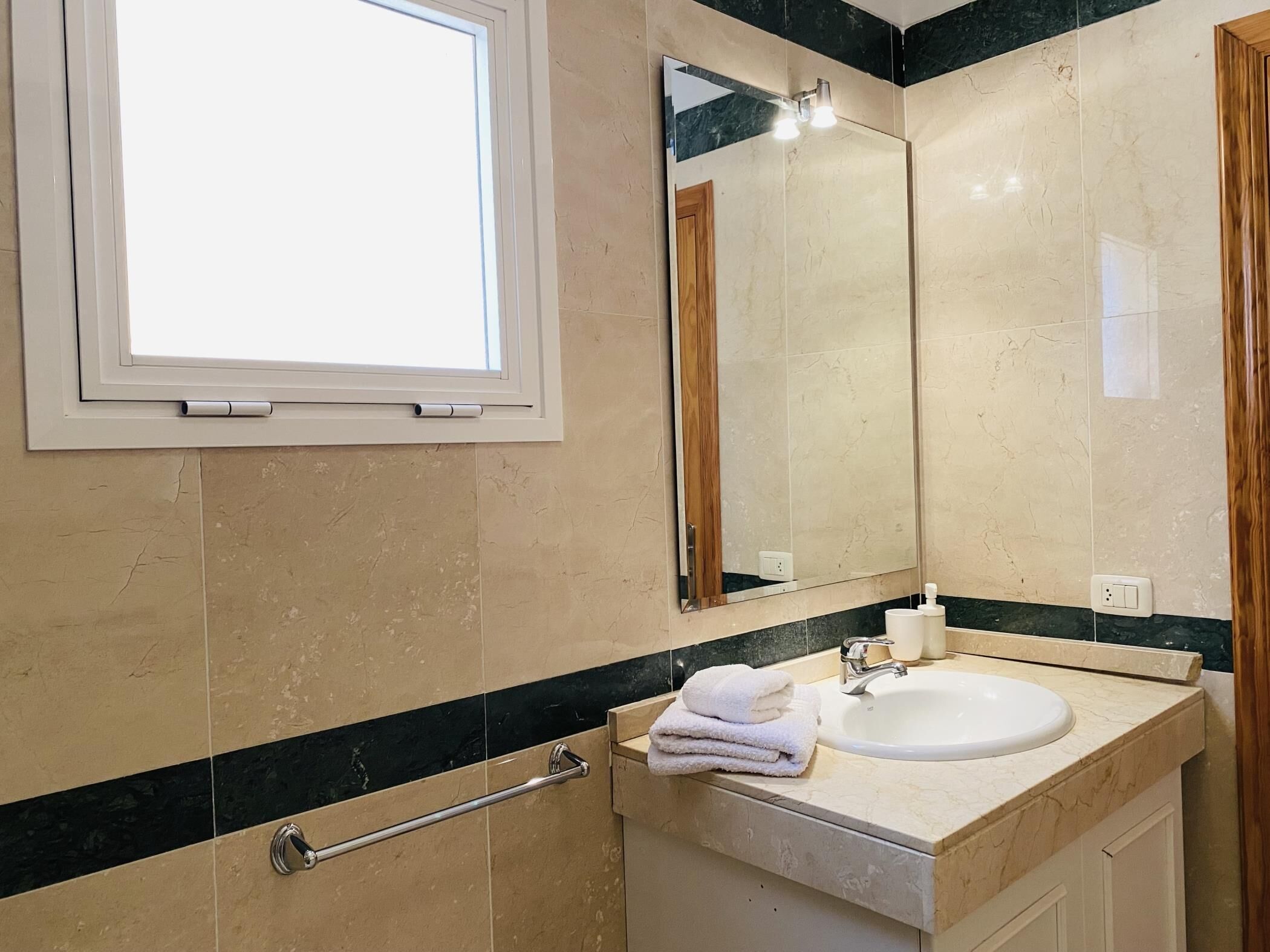 A bathroom with a window, a sink, a mirror, and a towel rack.