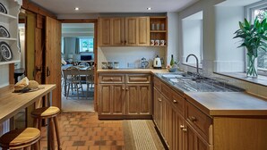 A modern kitchen with wooden cabinets, a large island with a sink, and a dining area visible through an open door. - Croft Meadows Farm -  5 bedroom, dog friendly cottage in rural Staffordshire  (Leek)