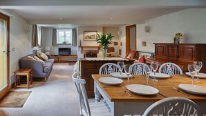 A spacious living area with a dining table set for four, a sofa, a television, and a kitchen area in the background. - Croft Meadows Farm -  5 bedroom, dog friendly cottage in rural Staffordshire  (Leek)