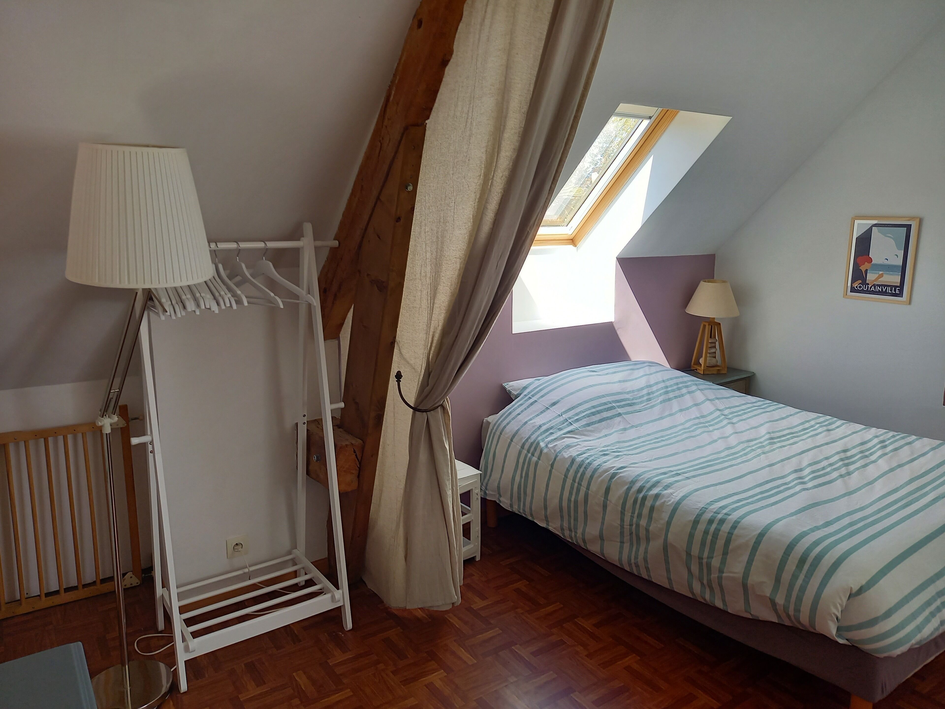 A bedroom with a bed, a hanging chair, a window with curtains, a lamp, and a poster on the wall.