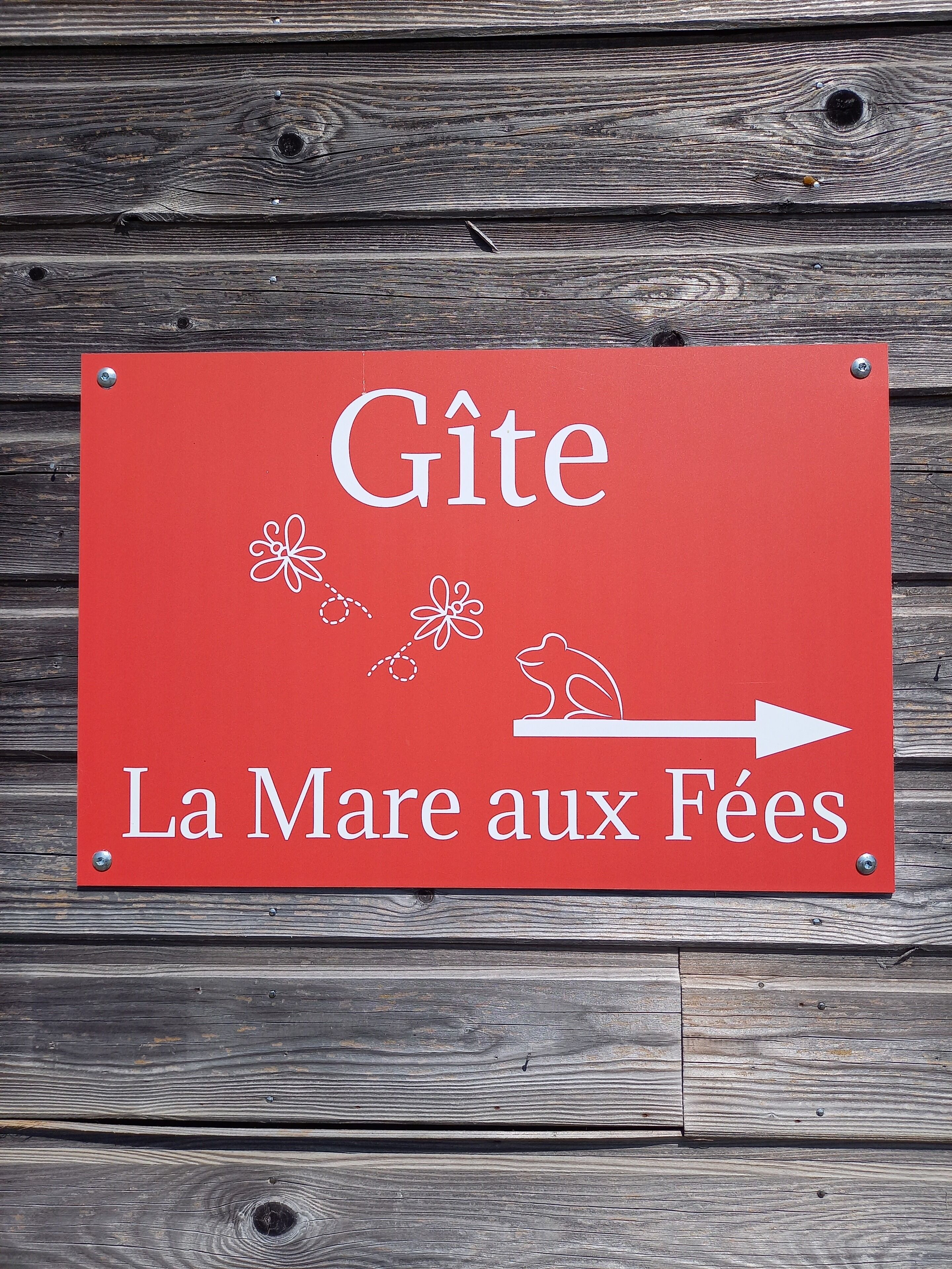 Een rood bord met witte tekst en een illustratie van een kikker, dat een richting aangeeft naar 'La Mare aux Fées'.