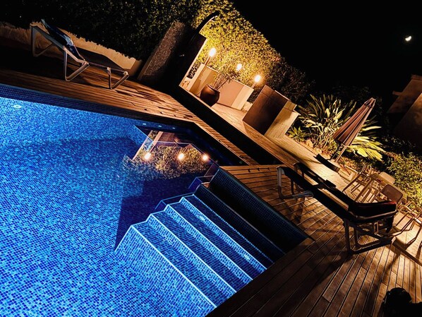 A nighttime swimming pool with steps leading into it, surrounded by lounge chairs and potted plants. - Modern luxury villa with pool and stunning sea views. (Binissafua)