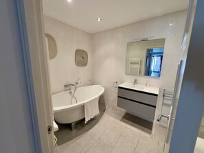 Un baño moderno con una bañera independiente, un lavamanos con espejo y un perchero para toallas.