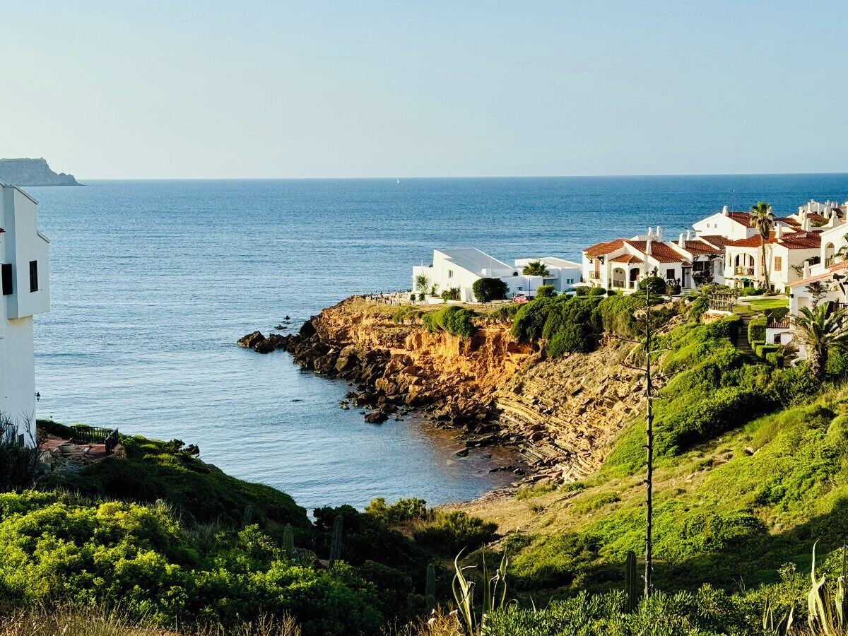 A coastal area with white buildings, rocky terrain, and a view of the sea.