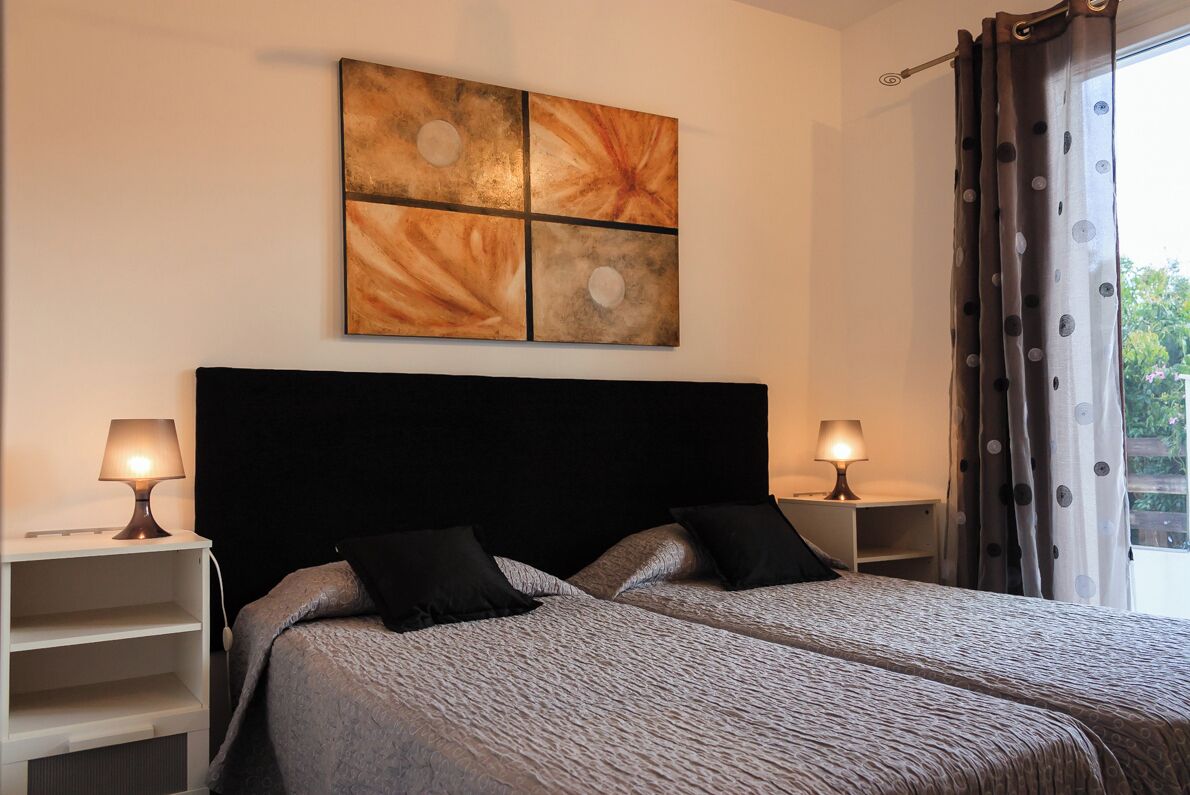 A double bed with a black headboard, two bedside tables with lamps, and a large abstract painting on the wall.
