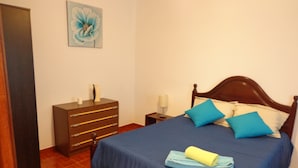 Ein Schlafzimmer mit einem hölzernen Bett, blauer Bettwäsche, einer Holzkommode und einem Gemälde an der Wand.