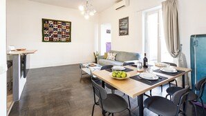 A dining area with a wooden table, black chairs, and a bowl of fruit. There is a grey sofa in the background and a blue cabinet to the right. - Penthouse with large terrace overlooking  Colosseum and  center of Rome. (Roma)