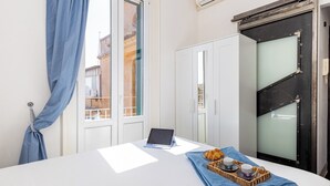 A room with a bed, a laptop, a tray with croissants and a cup, and a view of buildings through a window. - Penthouse with large terrace overlooking  Colosseum and  center of Rome. (Roma)