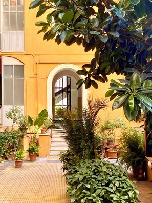 A courtyard with potted plants, a staircase, and a yellow building facade. - Penthouse with large terrace overlooking  Colosseum and  center of Rome. (Roma)