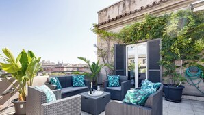 A rooftop terrace with wicker furniture, potted plants, and a view of the cityscape. - Penthouse with large terrace overlooking  Colosseum and  center of Rome. (Roma)