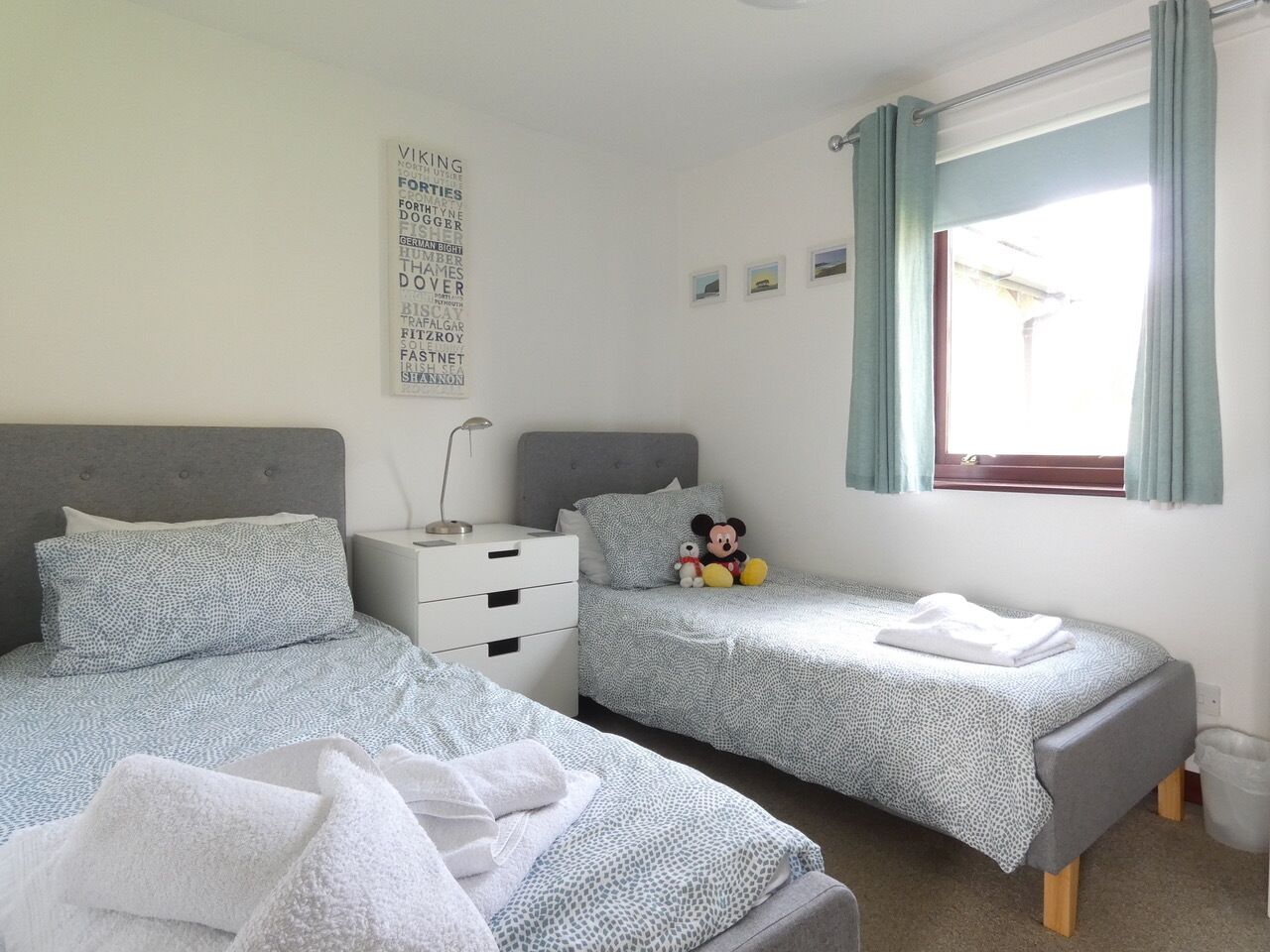 A bedroom with two beds, a nightstand, a Mickey Mouse plush toy, and a wall with a word cloud.