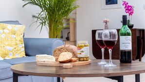 Un tavolo rotondo in legno con pane a fette, un barattolo di olive, due bicchieri da vino e una bottiglia di vino.