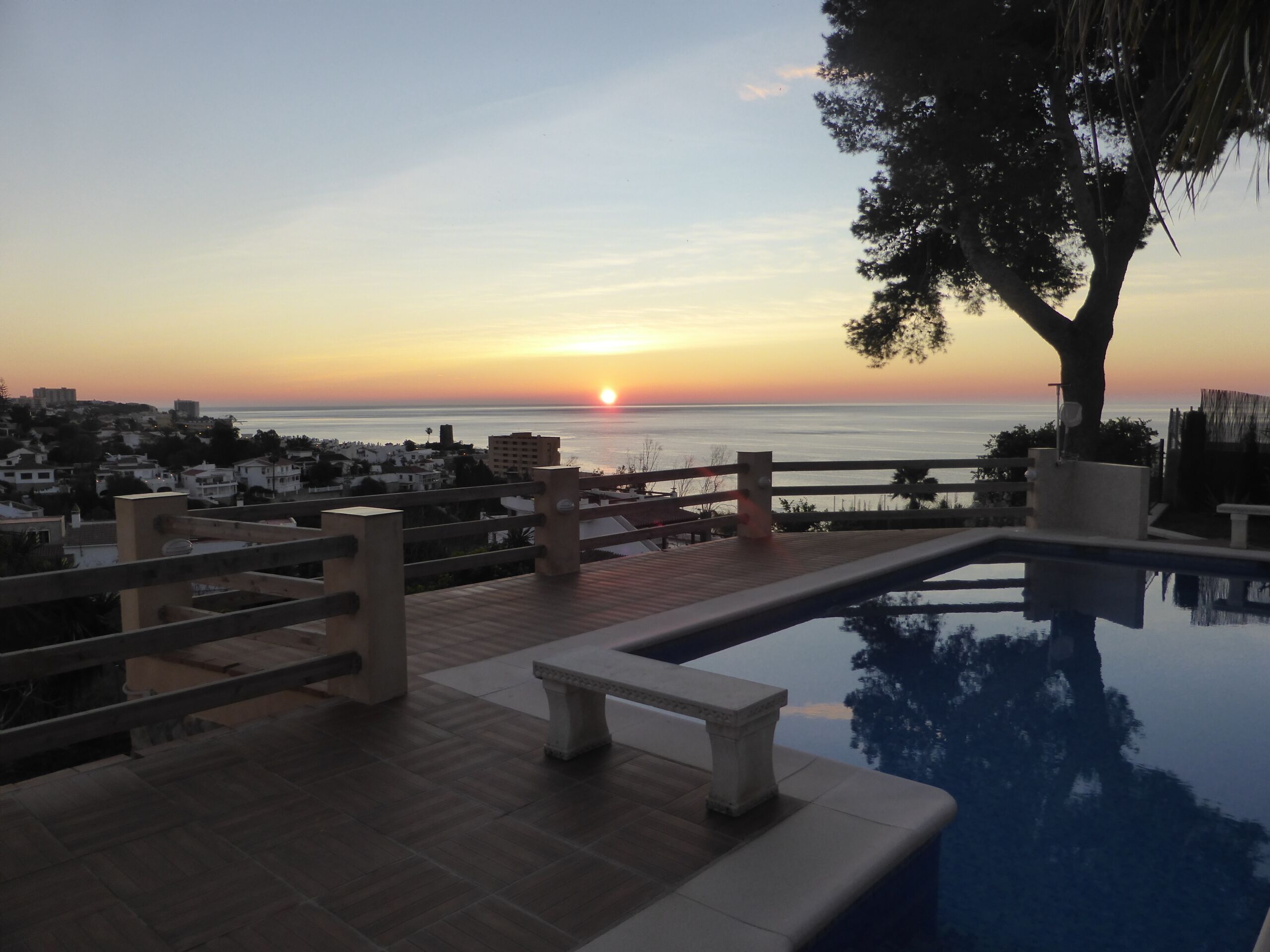 A pool area with a sunset view, wooden deck, and a bench.