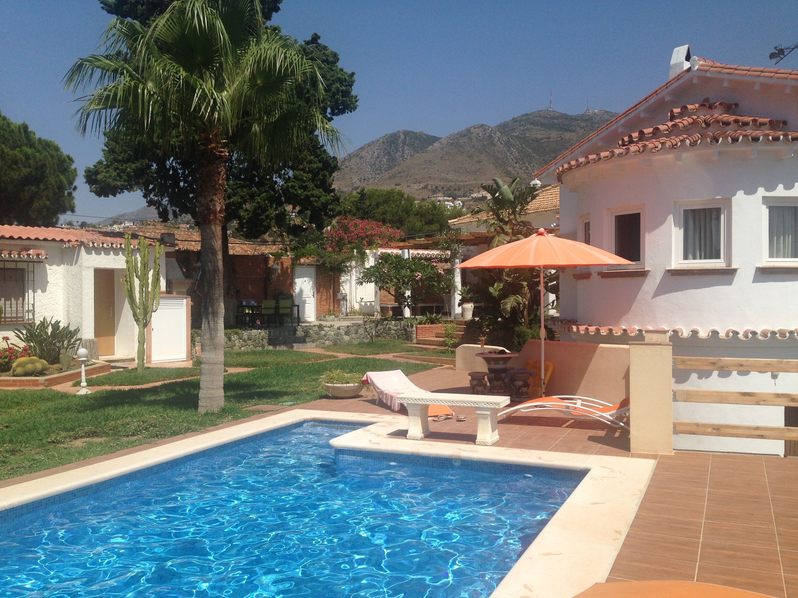 Ein Pool mit gefliestem Sonnendeck, umgeben von einem Garten mit Palmen und einem Berg im Hintergrund.