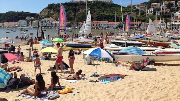 Une plage où des gens se prélassent au soleil et se baignent, entourée de bateaux et de parasols.