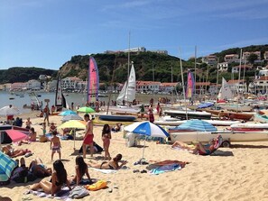 A beach with people sunbathing and swimming, surrounded by boats and umbrellas.