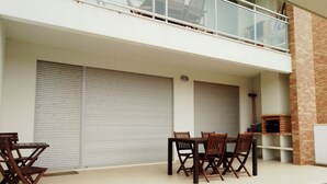 Un balcon avec une table et des chaises, une porte de volet fermée et une cheminée en briques.