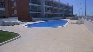 Une piscine avec des chaises longues et, au fond, un bâtiment doté de nombreux balcons.