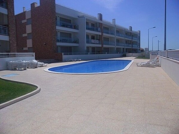 A swimming pool with lounge chairs and a building with multiple balconies in the background.