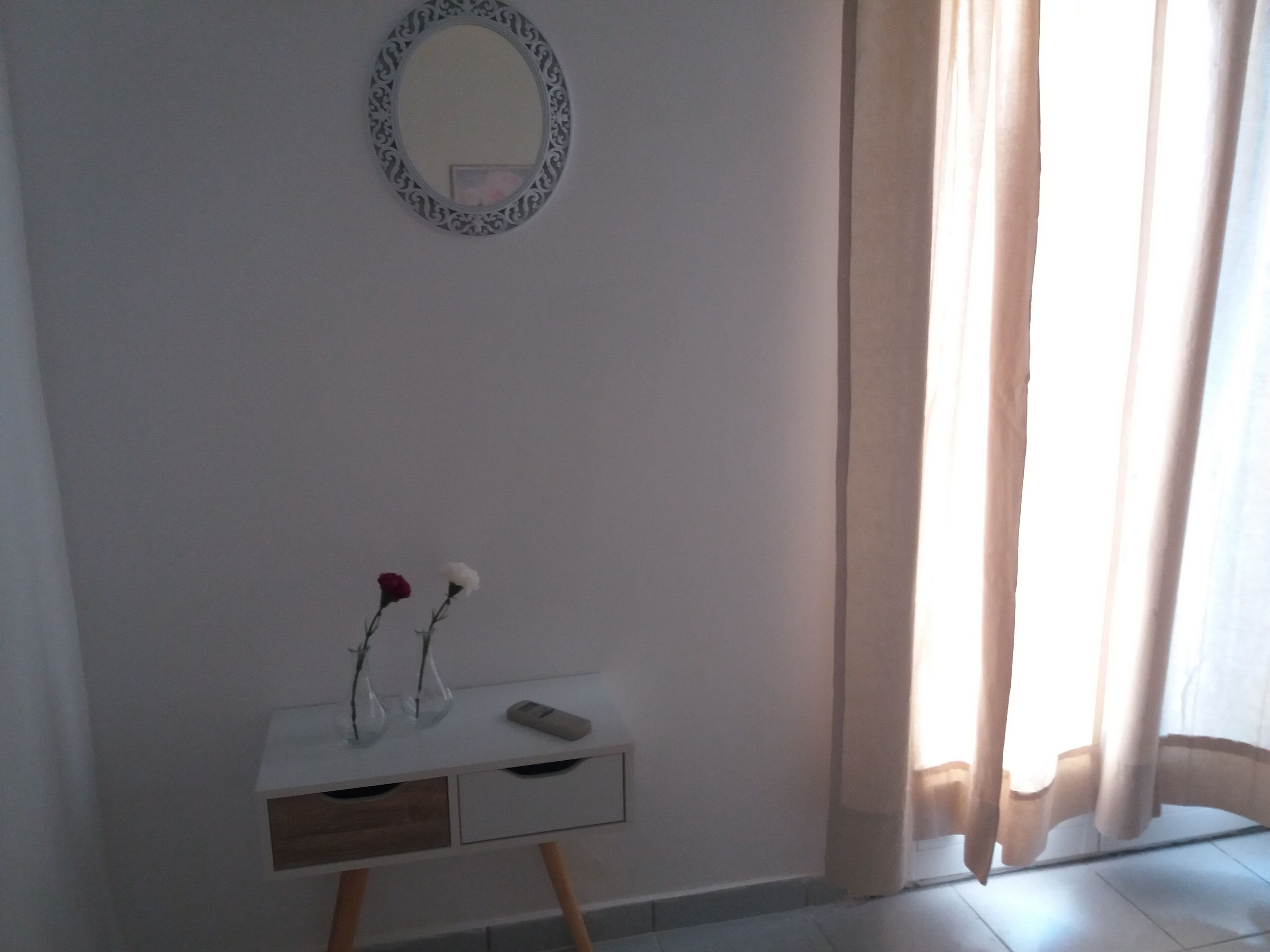 Una stanza con una scrivania bianca, uno specchio e due vasi con fiori.