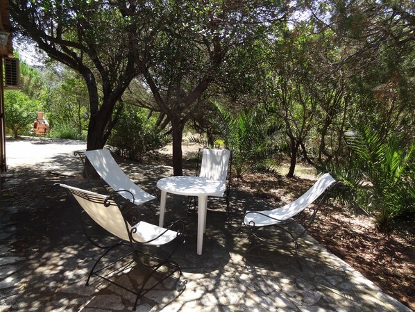 An outdoor seating area with a table and three chairs, surrounded by trees and a fire hydrant in the background.