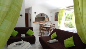 Ein gemütliches Wohnzimmer mit zwei braunen Sofas, jedes mit einem grünen Kissen, einem kleinen runden Tisch mit weißem Tuch und einem Fliesenboden.
