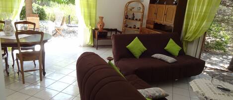 Un salon avec un canapé marron, des coussins verts, un meuble en bois et un coin repas comprenant une table et des chaises.