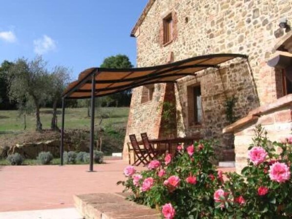 Un edificio de piedra con un porche cubierto, un banco de madera y flores rosadas.