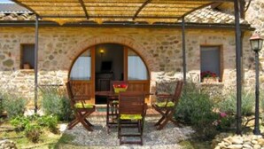 A stone building with a covered patio, two wooden chairs, and a table.