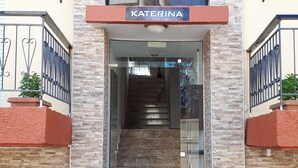 Hotellin sisäänkäynti, jossa on kyltti, jossa lukee ”KATERINA”, portaikko, joka johtaa sisälle, ja tervetulomat sisäänkäynnin alaosassa.