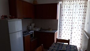 Kompakti keittiö, jossa on puukaapit, jääkaappi, liesi ja mikroaaltouuni. Siellä on ruokapöytä, jonka päällä on kuvioitu pöytäliina, sekä tuolit.