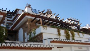 A building with a white facade, a wooden pergola on the upper floor, and a gated entrance. - Excellent house facing the sea in urbanization with community pool (Almuñécar)