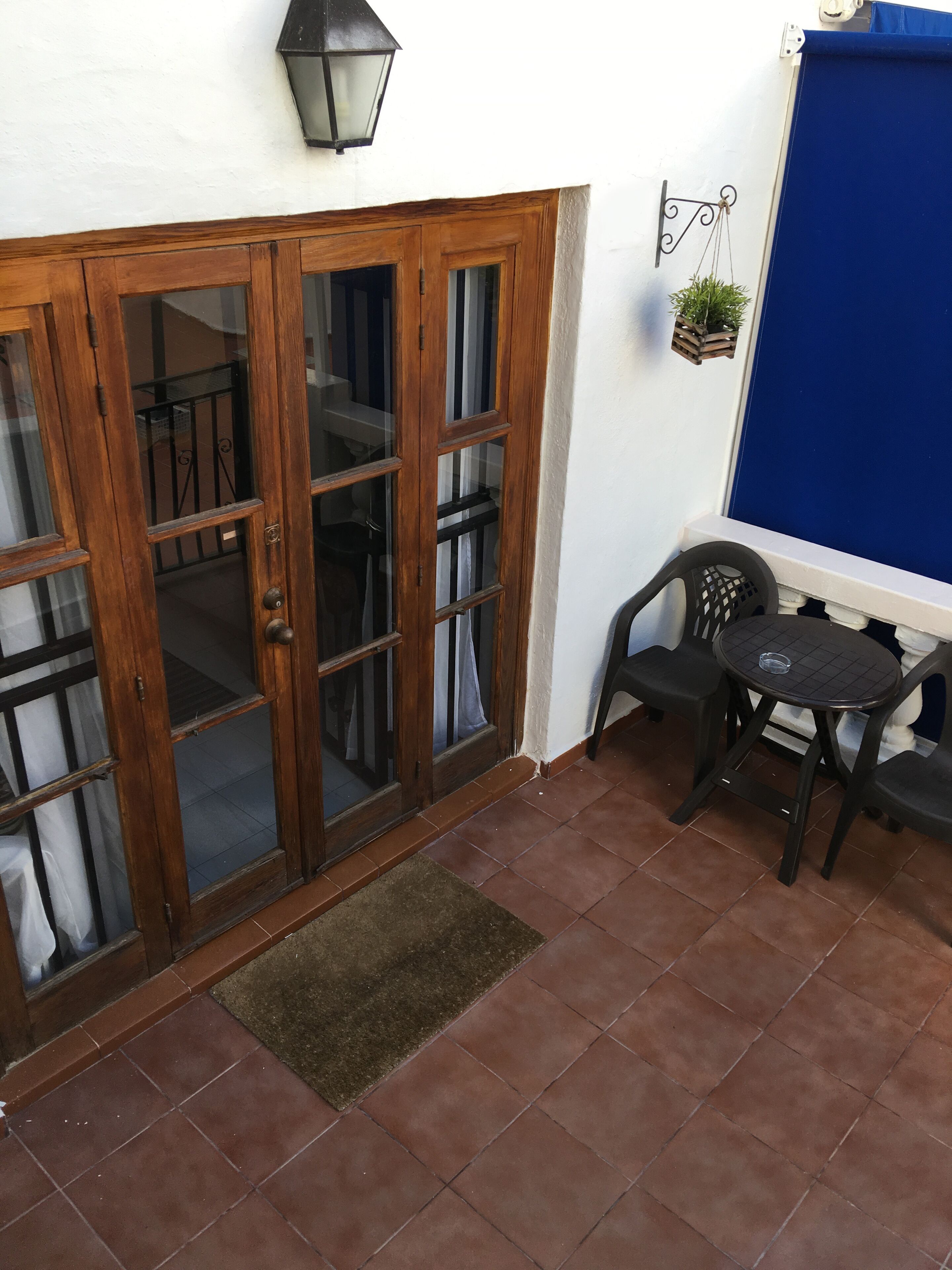 A wooden door with glass panels, a small round table with two chairs, a hanging plant, and a blue curtain.