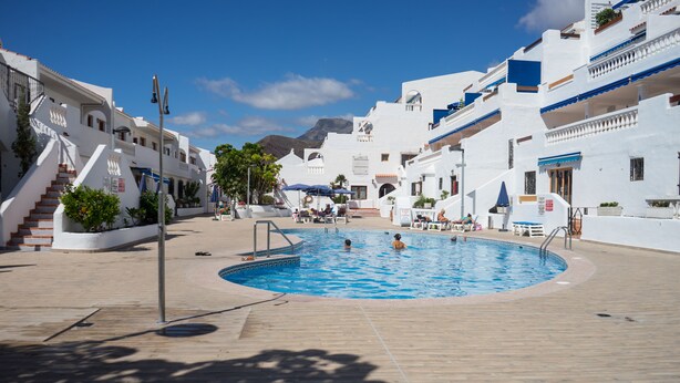 Ein Poolbereich mit einem klaren, blauen Pool, umgeben von weißen Gebäuden mit Balkonen und Treppen zum Pool.