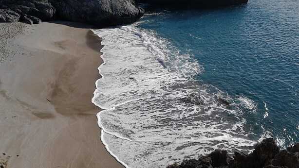 Une plage où les vagues se brisent sur le rivage, entourée de falaises rocheuses.
