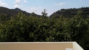 Un balcon agrémenté de deux chaises en bois et d’une petite table ronde, avec en toile de fond un paysage montagneux.